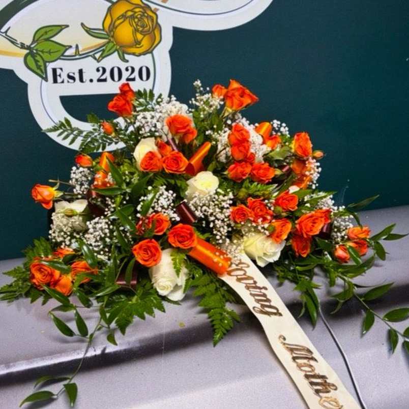 Orange and white rose arrangement with baby's breath on a casket
