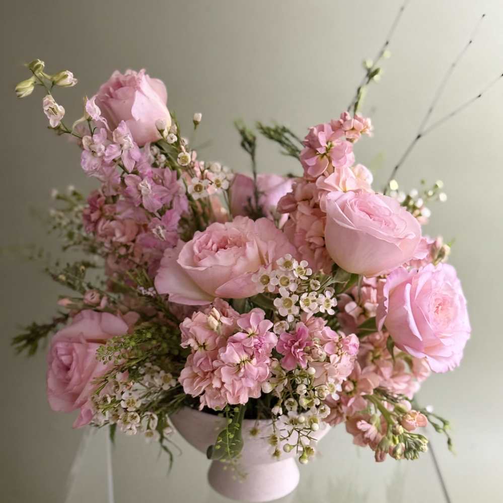 Pink roses and small blossoms arranged in a pale pedestal vase