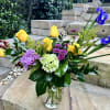 Mixed bouquet with yellow roses, purple blooms, and blue irises in a glass vase