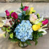 Mixed bouquet with blue hydrangea, pink roses, and yellow lilies in a glass vase