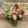 Bouquet of pink lilies, roses, and green button mums in a glass vase