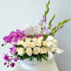 White roses and purple orchids arranged in a round hat box with a ribbon
