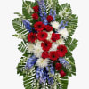 Tall standing spray with red roses, red gerberas, white mums, and blue delphinium on palm leaves