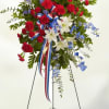 Tall red, white, and blue standing spray of flowers on a metal easel with a patriotic ribbon.