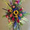 Tall multicolor standing spray with sunflowers, roses, carnations, and snapdragons on an easel