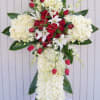 Standing cross of white flowers with red roses and white lilies on an easel