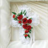 White lace cross with red roses and white filler flowers on a cream fabric background