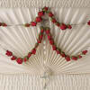 Red rosebud rosary draped across an ivory pleated casket interior with crucifix