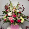 Pink and white floral arrangement in a pink box with a teddy bear topper
