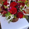 Low arrangement of red roses, orchids, and pink blooms with white frosted accents in a rustic bark container