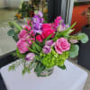 Low pink and purple flower arrangement with green hydrangea in a clear glass vase on a white table