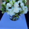 Low glass vase of white roses, lilies, and hydrangeas in a rounded arrangement