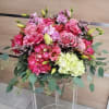 Large pink and cream flower arrangement with roses and hydrangeas in a low basket on a clear stand
