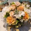 Low centerpiece of peach roses and white flowers in a clear glass vase