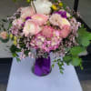 Round arrangement of pink and white mixed flowers in a glass vase with a purple ribbon