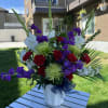 Large mixed floral arrangement in a white vase with purple, red, and white blooms