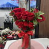 Red roses and carnations in a clear glass vase with a red ribbon.