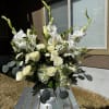 White floral arrangement in a white vase with roses and tall gladiolus