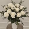 White roses arranged in a white vase with dark greenery