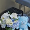 White and blue flower arrangement beside a light blue teddy bear