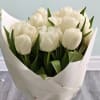Bouquet of white tulips wrapped in white paper in a glass vase