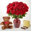 Red roses in a glass vase with a teddy bear and chocolates