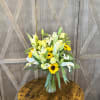 Bouquet of white lilies, yellow roses, and sunflowers in a clear glass vase