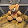 Brown teddy bear with red heart accents sitting on a wooden table
