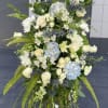Tall white floral standing spray with blue hydrangeas and greenery