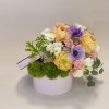 Pastel flower arrangement in a round pink box with purple and peach blooms