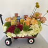 Flower arrangement in a red wagon with roses, hydrangeas, and alphabet blocks