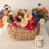 Mixed bouquet in a wicker basket with a candle beside it