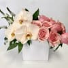 Pink roses and white orchids arranged in a white square vase