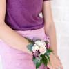 Person wearing a small wrist corsage with pale roses and purple flowers