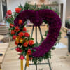 Heart-shaped floral wreath with purple blooms and orange roses on an easel