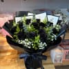 Bouquet of black roses with white filler flowers wrapped in glossy black paper and ribbon