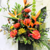 Tropical floral arrangement with orange bird-of-paradise and coral roses in a black vase