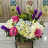 Low wooden box arrangement with blue hydrangeas, white blooms, pink roses, and purple accent flowers.
