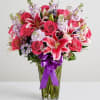 Pink roses and lilies in a clear glass vase with a purple ribbon