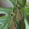 Gold teardrop earrings with fern cutouts on a large green leaf