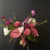 Asymmetrical arrangement of pink and purple flowers in a gold pedestal vase against a dark background