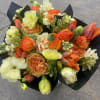 Bouquet of orange, cream, and pale yellow flowers wrapped in black paper