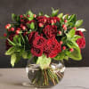 Red roses in a clear glass vase with green foliage and red berries