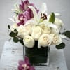 White roses and lilies arranged in a square glass vase with purple orchids