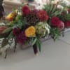 Low centerpiece of red and yellow roses, mums, protea, herbs, and artichoke in a rustic rectangular box