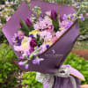 Purple-wrapped bouquet of pink, lavender, and yellow flowers with a ribbon tie