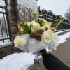 White rose bouquet with pinecones and mesh wrap held outdoors in snow