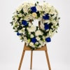 Heart-shaped floral wreath of white flowers with blue roses on a wooden stand
