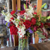Red roses and lilies arranged in a glass vase with ribbon curls