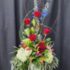 Tall floral arrangement with red roses, blue delphinium, and white hydrangeas